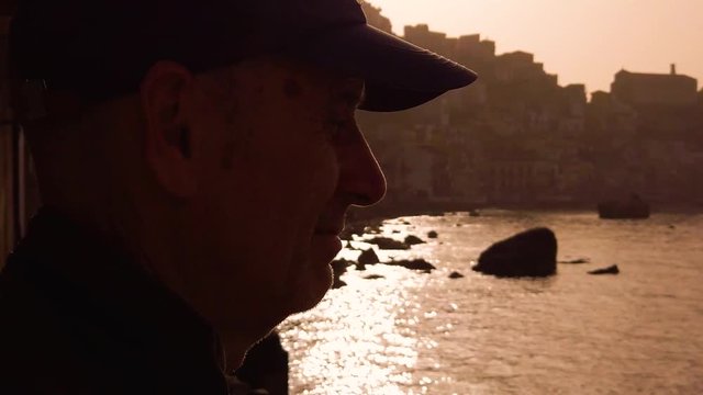 Silhouette di un vecchio pescatore con cappello osserva il mare al tramonto. vicino gli scogli.