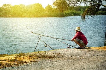 Fishing activities. fisherman middle-aged man red shirt with a straw hat and three fishing rods on natural water swamp background landscape.