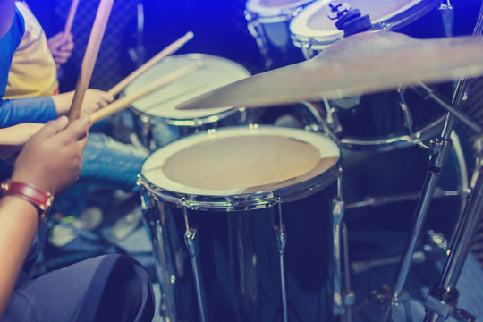 hands of teacher with wooden drumsticks guiding boy in drum learning tutorial in recording studio at music academy