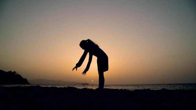 Silhouette di una bambina che fa passi di danza al tramonto sulla spiaggia di fronte al mare.