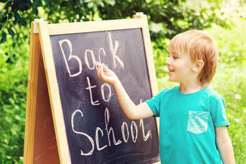 Happy smiling boy is going to school for the first time. Back to school. Kid writes on blackboard. School, kid, education.