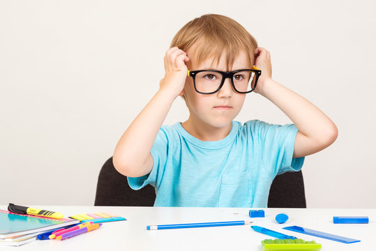 Serious kid in eyeglasses is sitting at a desk. Little child writing with colorful pencils, indoors. Elementary school and education. Ready for school. Back to school.