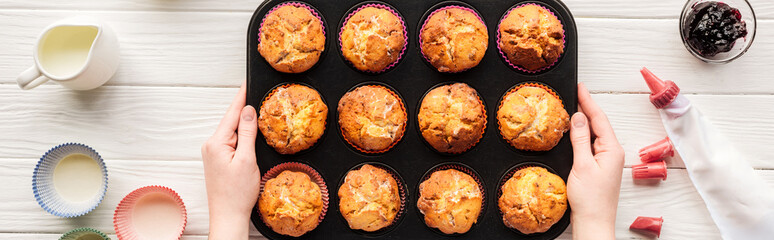 panoramic shot of woman holding muffin pan on table with baking tools