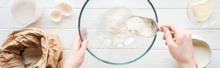 panoramic shot of woman with scoop putting flour in bowl while cooking on table