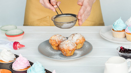 Cropped view of woman decorating cupcakes with powdered sugar isolated on grey