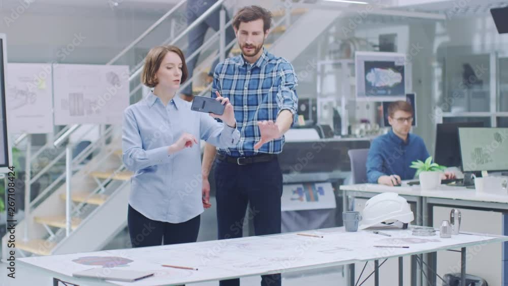 Aufkleber In the Industrial Engineering Facility: Female Designer with Chief Engineer Uses Smartphone for Augmented Reality App to Manipulate Engine Design Technical Drafts in 3D. High Tech Office. Mock-up