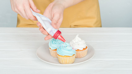 Fototapeta na wymiar cropped view of woman decorating cupcakes with icing bag