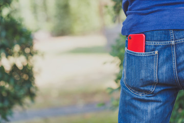 Red smart phone in pocket of blue jeans.