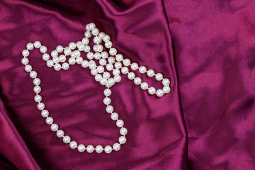 Pearl necklace on purple satin fabric background