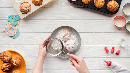 partial view of woman decorating cupcakes with powdered sugar on table with baking tools