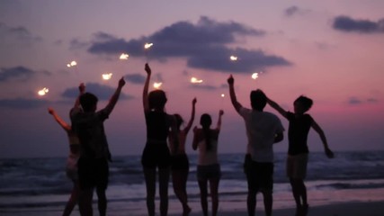 Silhouette of Asian teen group dancing and playing firework seaside together in beach summer with sunset background. Young asia happy emotion and anniversary celebration. - Powered by Adobe