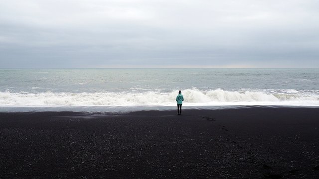 czarna plaża islandia black beach czarny piasek ocean osoba patrzy pochmurne niebo
