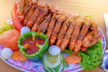 Tasty appetizing fried shrimps prawns with spices on pan with ingredients on yellow background. Selective focus