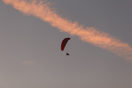  At the top in the sky flying paraplane with a paratrooper. In the sky a beautiful line of clouds at sunset in the form of a road. The concept of freedom, sport, healthy lifestyle and travel.