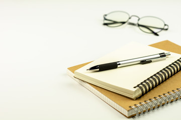 pen on diary book and glasses on white desk background.