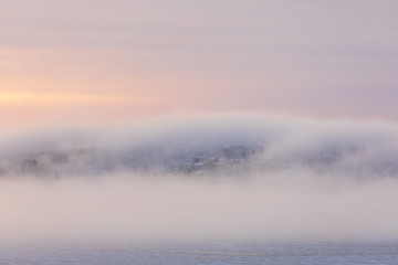 Thick fog at sunrise over hill and city buildings