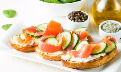 Fototapeta na wymiar Salmon, cucumber and cream cheese bruschetta. Italian tapas, antipasti with vegetables, herbs and oil on grilled ciabatta and baguette bread. Sandwich.