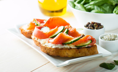 Salmon, cucumber and cream cheese bruschetta. Italian tapas, antipasti with vegetables, herbs and oil on grilled ciabatta and baguette bread. Sandwich.