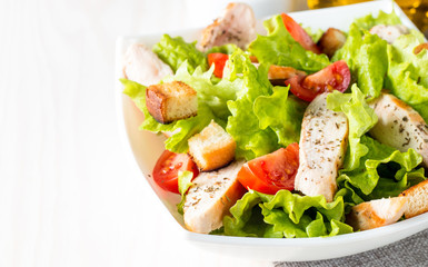 Fresh salad made of tomato, ruccola, chicken breast, eggs, arugula, crackers and spices. Caesar salad in a white, transparent bowl on wooden background