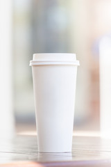 Disposable coffee cup and smartphone on wooden table at cafe terrace blurred background