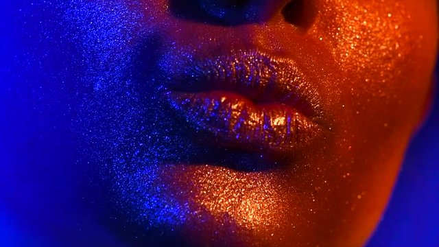 Beautiful sexy lips, kiss. Fashion model woman kiss lips in bright sparkles, colorful neon lights. Trendy glowing gold skin makeup. Slow Motion 4K UHD video footage. 3840X216