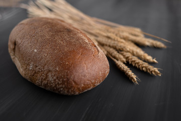 a loaf of dark bread on the table, next to it is wheat in an ear