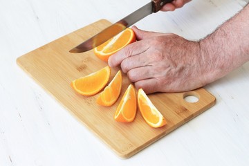 Hand slicing orange on wooden board
