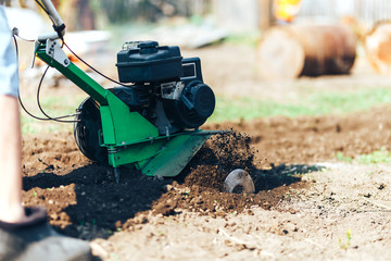 close up photo of young farmer gardener cultivate ground soil rototiller , tiller tractor,...