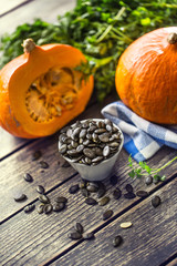 Roasted pumpkin seeds with raw pumpkins on wooden table