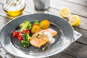 Roasted salmon fillet broccoli tomatoes and fried potatoes with dill cream sauce