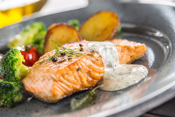 Roasted salmon fillet broccoli tomatoes and fried potatoes with dill cream sauce