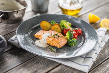 Roasted salmon fillet broccoli tomatoes and fried potatoes with dill cream sauce