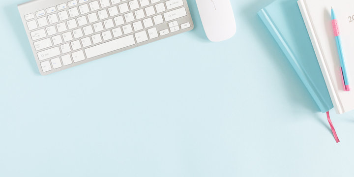 Female home office workplace with keyboard, notepad, notebook on pastel blue background. Business minimal concept for women. Flat lay, top view, copy space