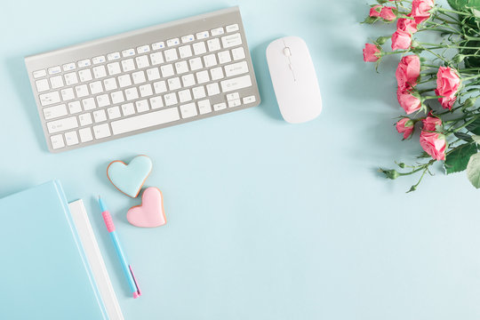 Composition Valentine's Day. Female home office with keyboard, notepad, rose flowers and ginger cookie in shape heart on pastel blue background. Flat lay, top view, copy space