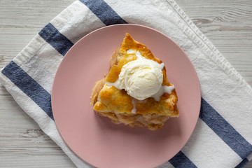 Slice of homemade apple pie with vanilla ice cream on a pink plate, top view. From above, overhead, flat lay.