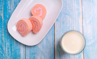 Strawberry cake roll on white dish and soy milk with blue wood background.