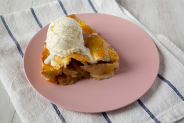 Slice of homemade apple pie with vanilla ice cream on a pink plate, side view.