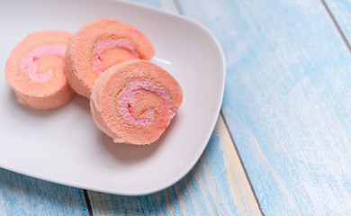 Strawberry cake roll on white dish with blue wood background.