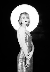 Cute face blond girl with red lips and vintage style hairstyle, wearing a golden sparkling dress with a halo behind her head. Isolated on black. Clean, healthy skin. Black and white