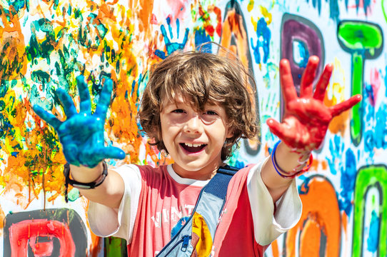 Happy cute boy with painted paint palms outstretched ahead. Happy summer holidays. School education. Children's summer camp outdoors