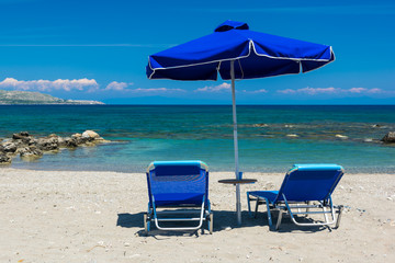 Sun beds, lounge chairs and an umbrella on the beach, on the seashore.