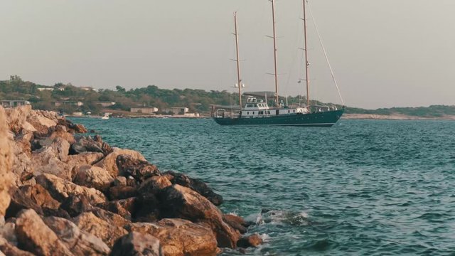 View of a boat floating on the blue-green sea with white sand many rock on the beach around with high cliff and mountain with blue sky background, .