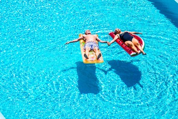 Old people senior couple relax and sleep on the blue swimming pool clear water lay down on trendy coloured inflatabler mattress lilos and taking hands with love for forever together lifestyle concept