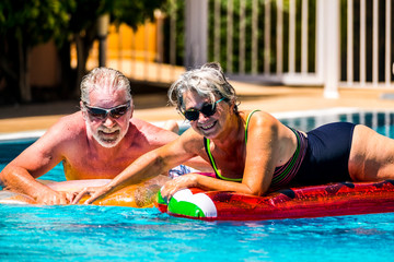 Happy joy cheerful people adult senior couple have fun in the swimming pool with trendy coloured lilos mattress on a blue water in hotel resort for summer holiday vacation lifestyle