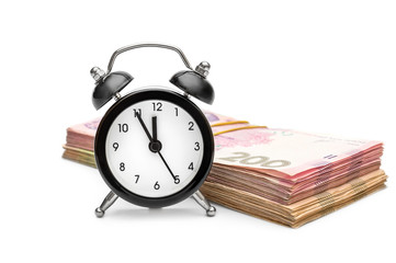 Alarm clock with hryvnia bundles on white background.