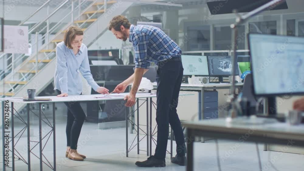 Poster in the industrial engineering facility: young female designer works with chief industrial engineer, 