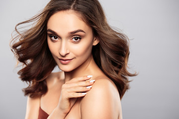 Naklejka premium Brunetka dziewczyna z zdrowe włosy kręcone i naturalny makijaż. Piękny model kobiety z falowaną fryzurą. Pielęgnacja i uroda