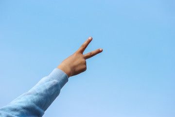 backside of a victory sign from a young girl hand with blue sky as background.