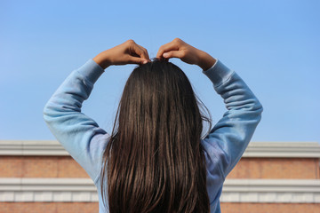 back side of a young girl who making heart shape by body language.