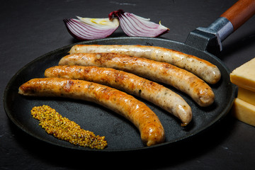 big frying pan with fried thin sausages and granular mustard